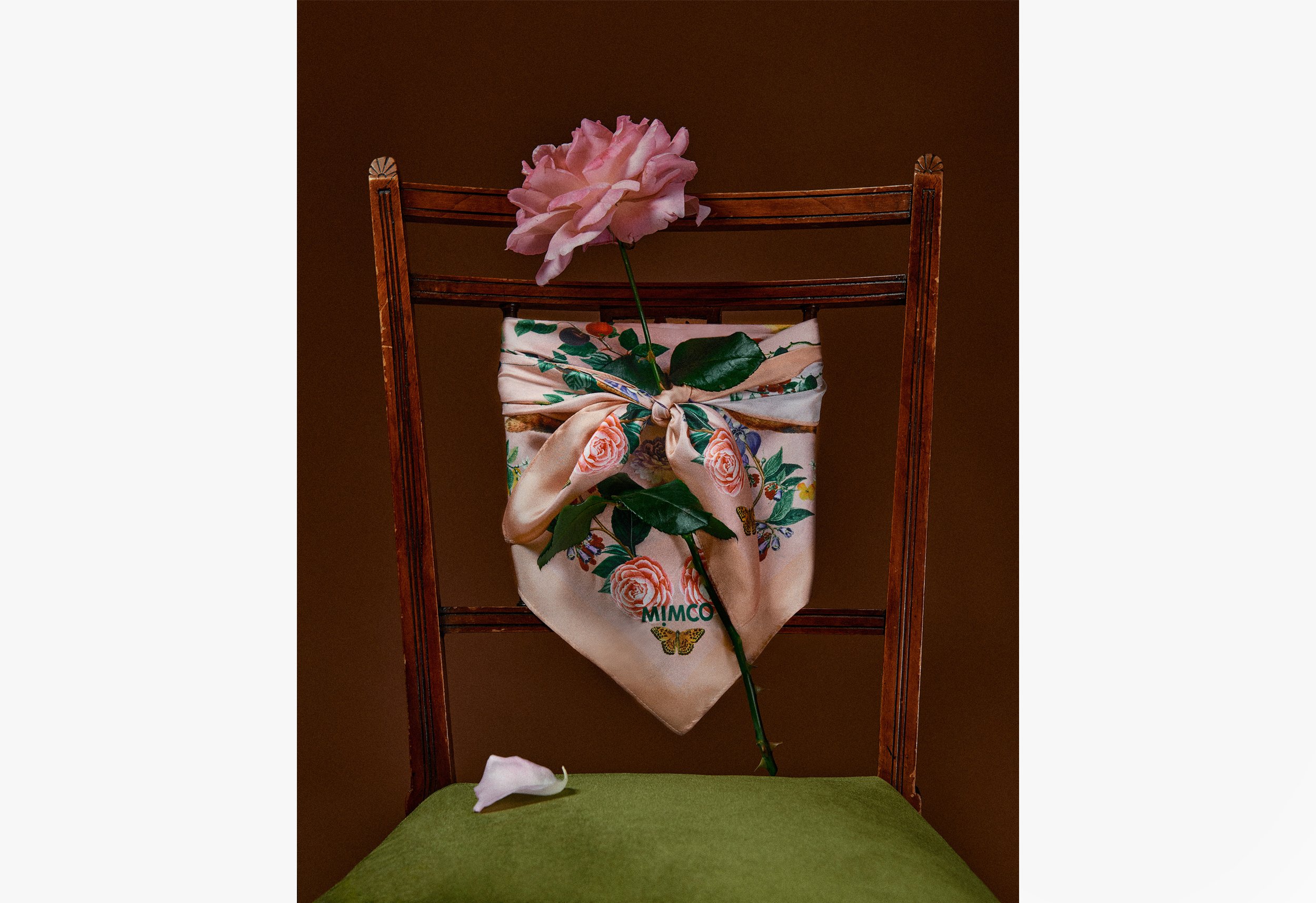 Still life featuring a pink rose, a patterned silk scarf, and a green chair, creating a visually appealing and artistic composition.