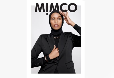 Model in black blazer and hijab with gold chain jewelry against a grey background by Sophie Pike