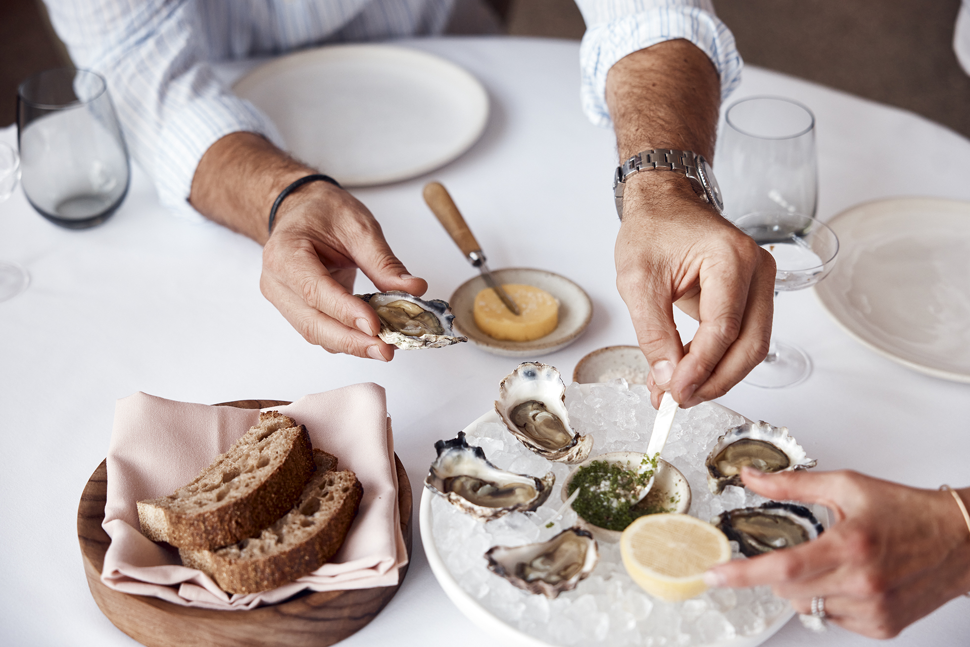 Overhead shot of two people preparing and eating oysters with bread at a restaurant, showcasing a fresh and gourmet seafood experience.