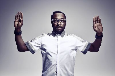 Portrait of an adult male with beard and glasses wearing a white shirt with gray collar and cuffs, raising both hands in a photo studio.