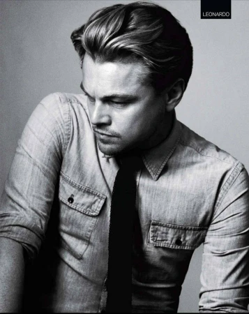 Black and white portrait of Leonardo DiCaprio in a denim shirt and dark tie, gazing downward in a grey gradient background.