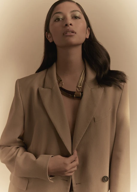 Portrait of an adult woman wearing a beige blazer and a statement necklace with a neutral-toned background in a fashion style image.