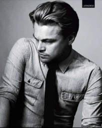 Portrait of Leonardo DiCaprio with styled hair wearing a denim shirt and dark tie against a plain grey background
