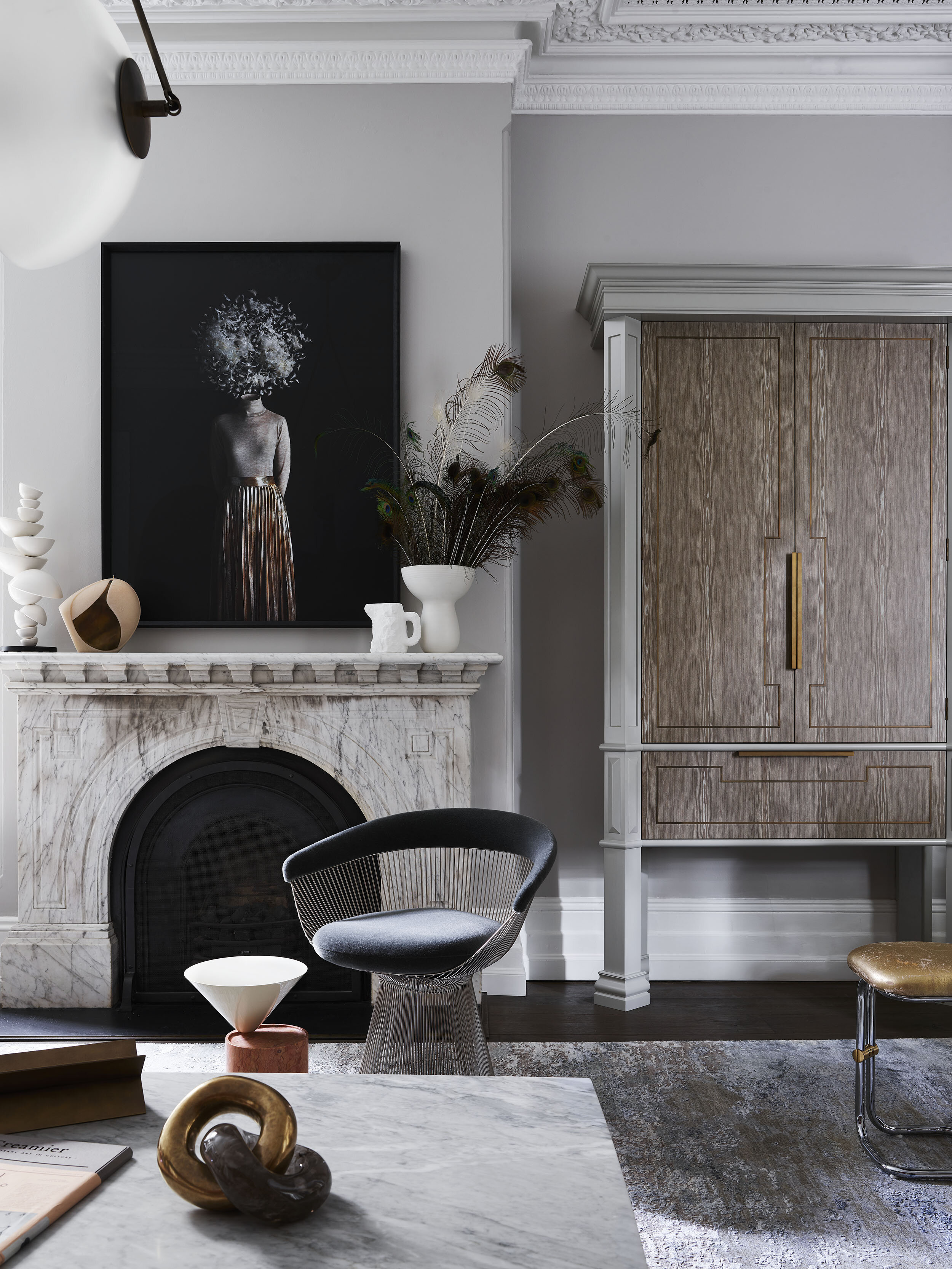 Living room interior with a marble fireplace, a framed portrait, stylish armchair, coffee table, decorative objects, and wood cabinet.