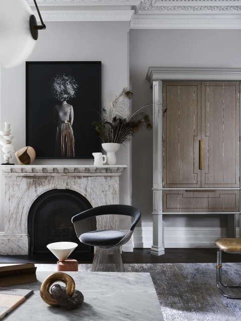 Living room interior with a marble fireplace, a framed portrait, stylish armchair, coffee table, decorative objects, and wood cabinet.