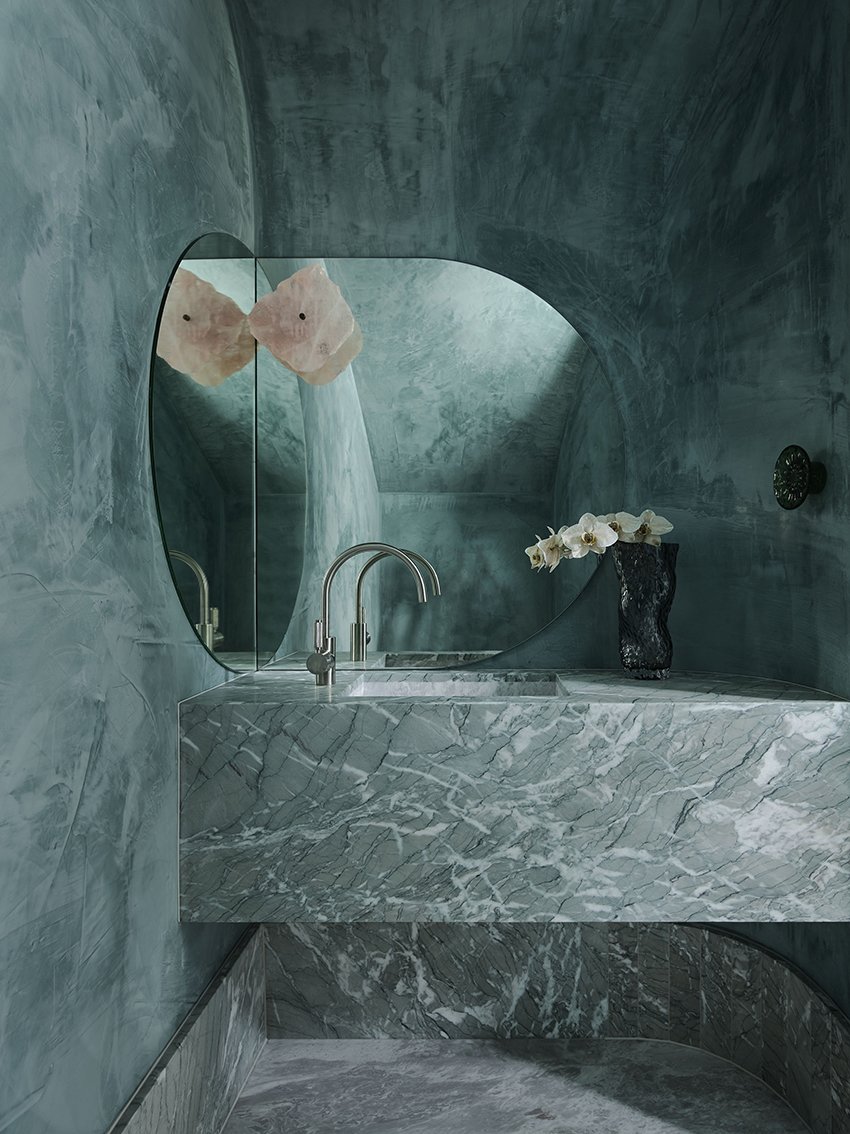 Modern bathroom with green marble vanity, basin faucet, mirror, and orchid, providing a luxurious and contemporary interior design aesthetic.