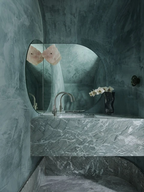 Modern bathroom with green marble vanity, basin faucet, mirror, and orchid, providing a luxurious and contemporary interior design aesthetic.