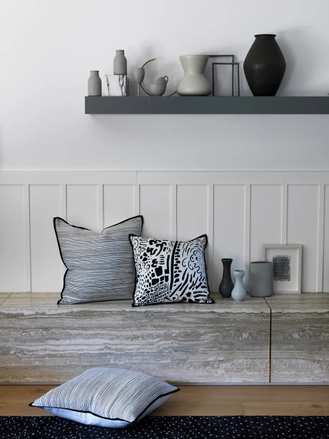 Still life featuring decorative cushions and ceramic vases displayed on a light-grey ledge against a white wall backdrop, indoors.