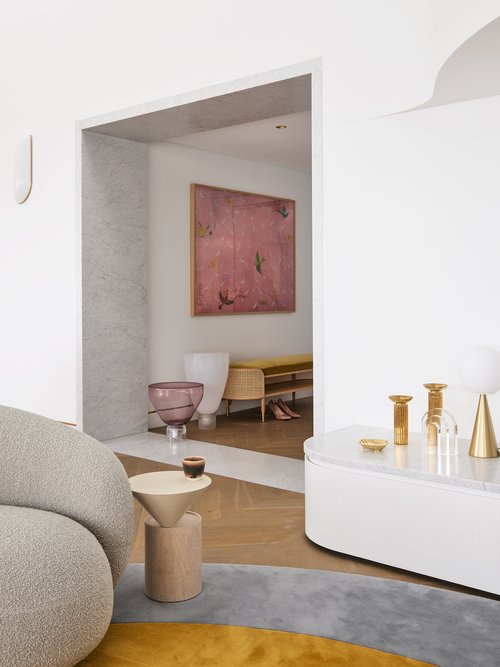 Interior view of living room with gray textured sofa, small round side table, and view into room with pink abstract painting.