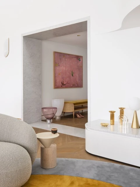 Interior view of living room with gray textured sofa, small round side table, and view into room with pink abstract painting.