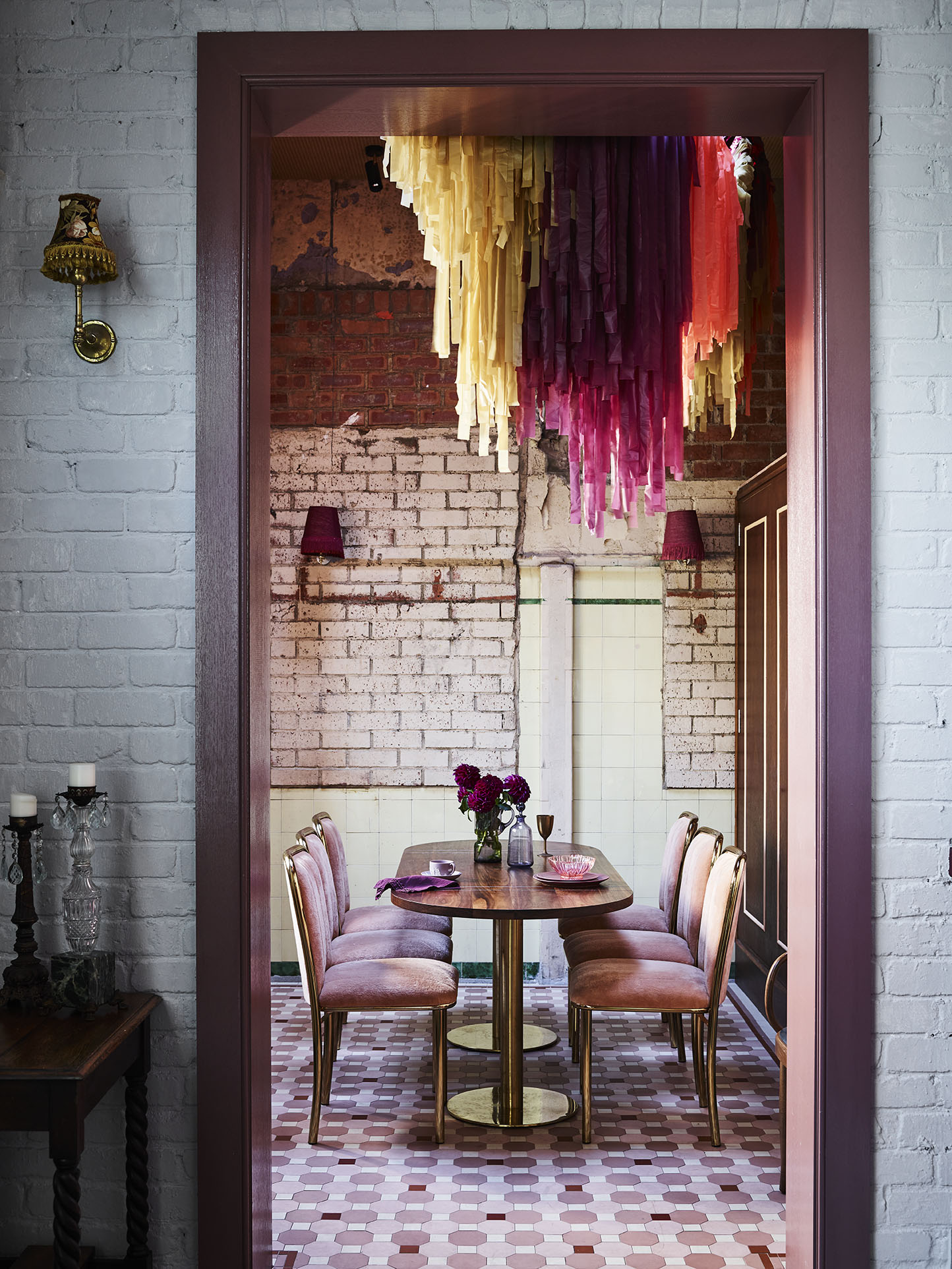 Dining room with decorative streamers hanging from the ceiling, set with a dark wood table, pink velvet chairs and brick walls.