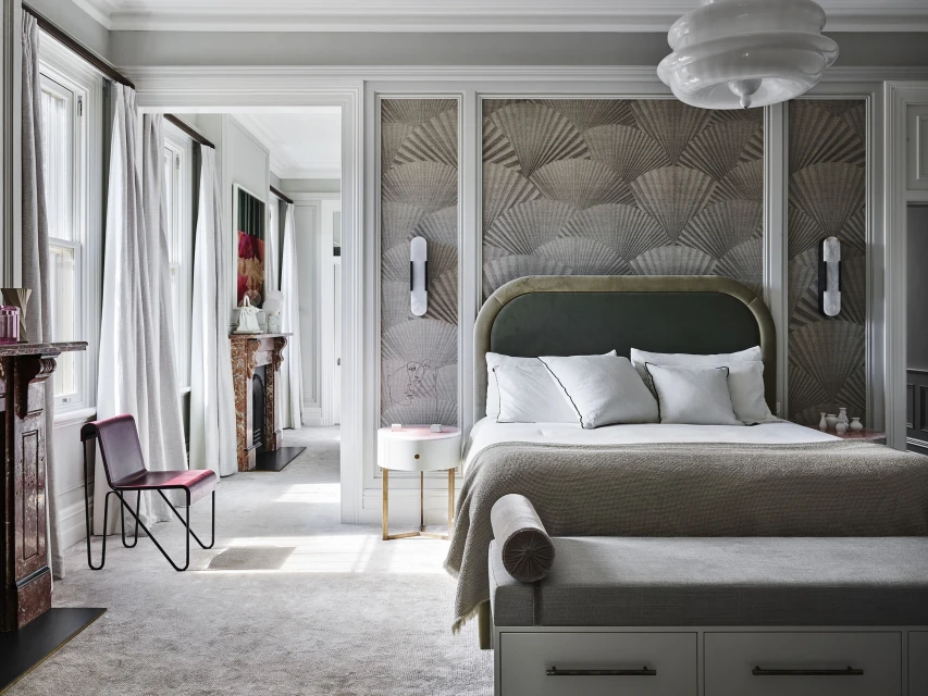 Elegant bedroom interior showcasing a bed with a patterned headboard, white linens, and stylish decor in a well-lit, neutral-toned space.