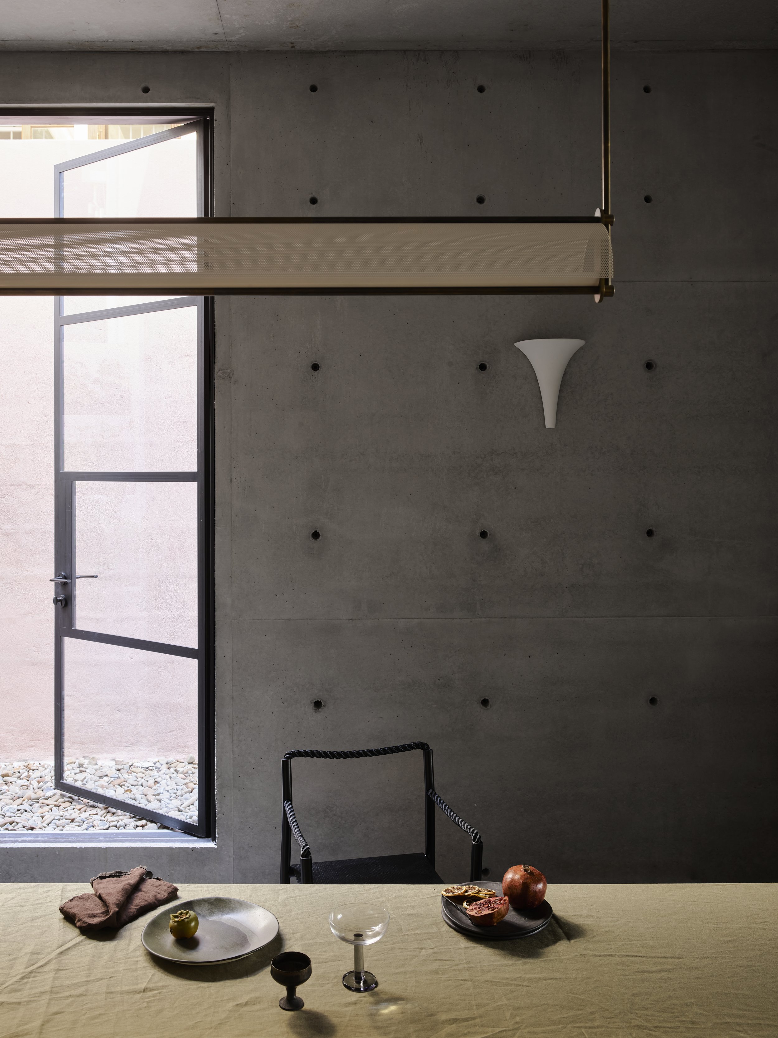 Indoor dining area featuring a table with place settings, modern lighting fixture, an open door, and a concrete wall.