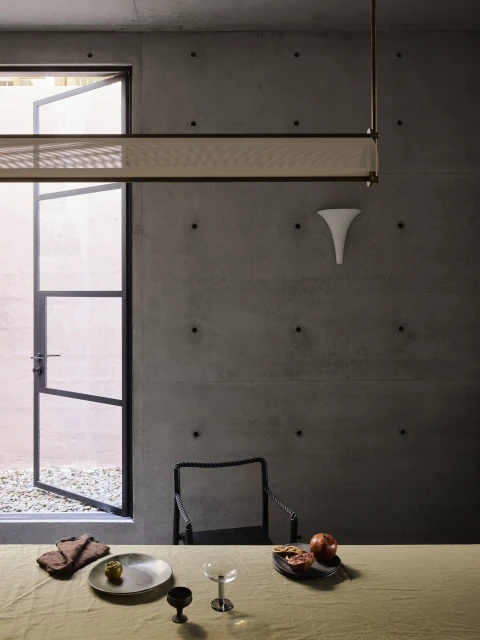 Indoor dining area featuring a table with place settings, modern lighting fixture, an open door, and a concrete wall.