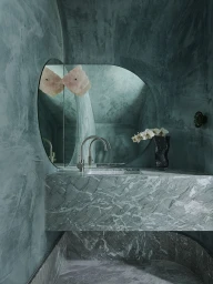 Modern teal marble bathroom interior with arched textured walls and a curved mirror reflecting white flowers in a vase