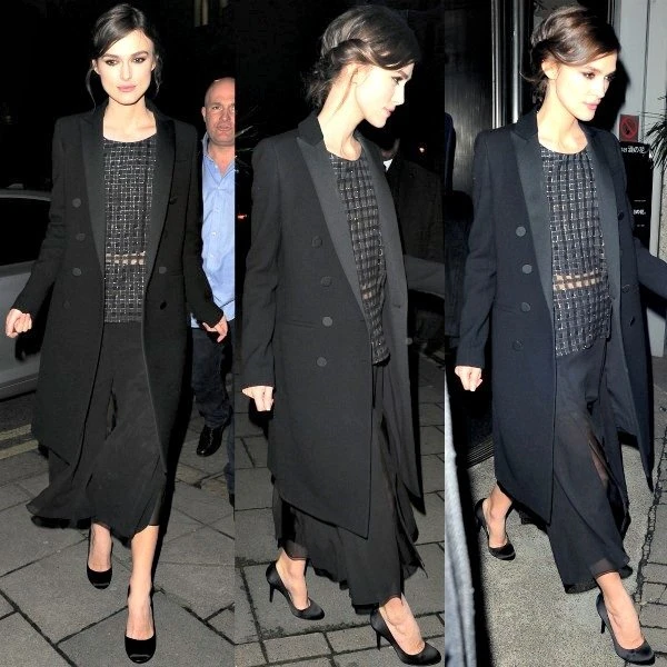 Keira Knightley wearing a black double-breasted coat, a patterned top, and flowing black pants. She is seen on a city street at night.