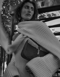 Black and white portrait of a woman in a ribbed knit sweater holding a handbag with a prominent YSL logo, styled by Amiee Hershan