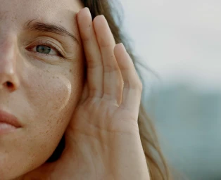 Close-up portrait of a woman with freckles holding her hand up near her face by photographer Saskia Wilson