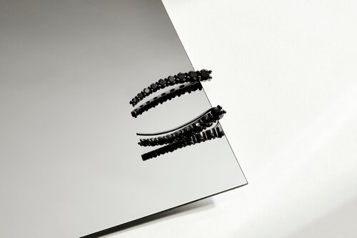 Still life of two black hair clips on a mirror surface against a white background, showcasing fashion and beauty accessories.