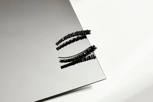 Still life of two black hair clips on a mirror surface against a white background, showcasing fashion and beauty accessories.