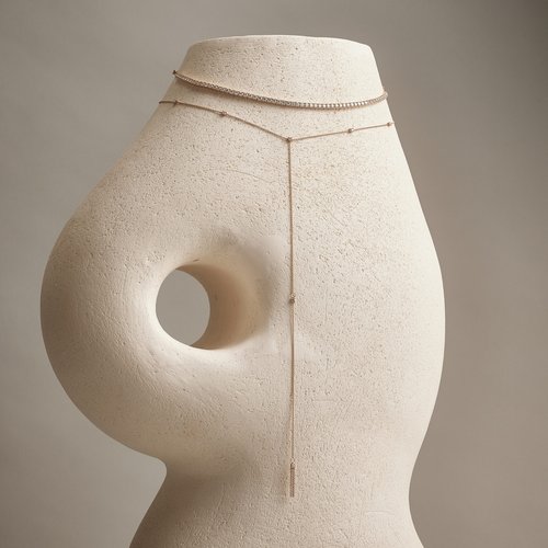 Elegant tennis necklace and Y-necklace displayed on a textured form against a soft gray backdrop in a fashion or jewelry product shot.
