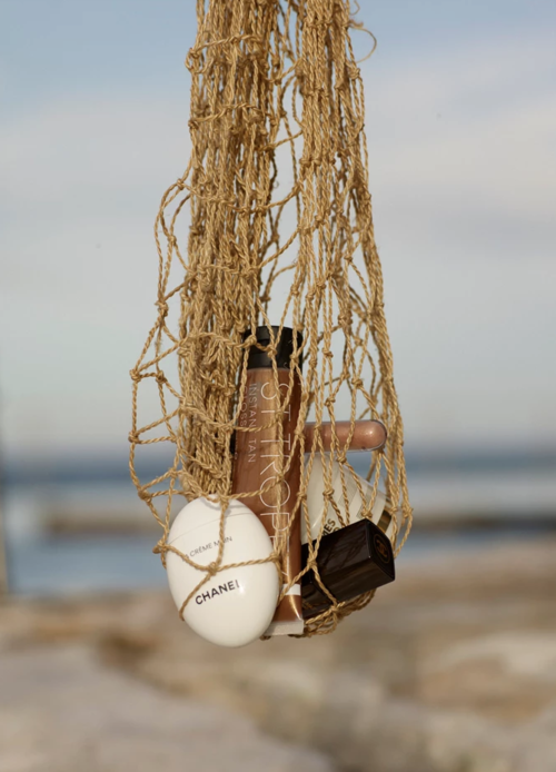 Cosmetic products displayed inside a woven net, featuring items like lotions and bronzers, set against a blurred outdoor background.