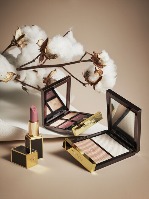Cosmetic still life shot featuring lipstick, compacts, and cotton branches on a neutral backdrop, highlighting beauty and elegance.