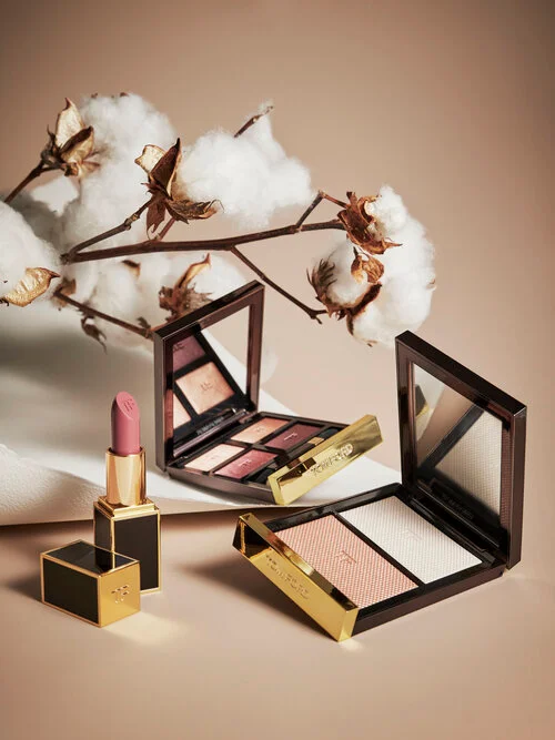 Cosmetic products featuring two eyeshadow palettes and a pink lipstick with cotton stems styled on beige backdrop
