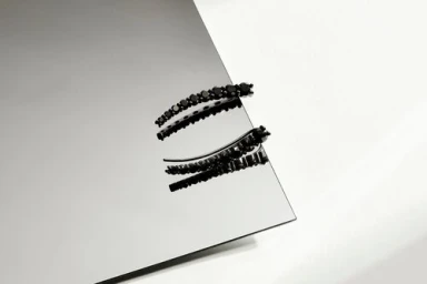 Two curved black crystal ear crawler earrings placed on a reflective metallic surface next to a white background.