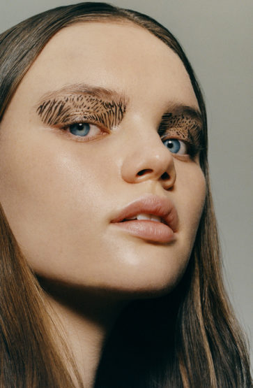 Close-up of a woman's face with dramatic feather-like makeup applied to her eyebrows, showcasing a creative beauty concept.
