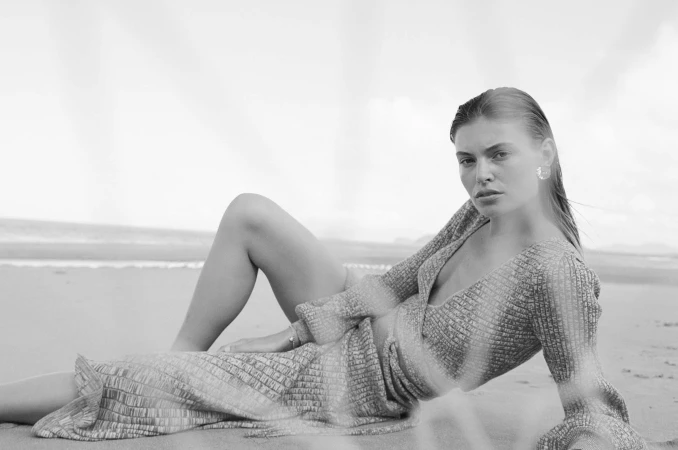 Monochrome fashion photography of a woman reclining on a sandy beach wearing a patterned wrap dress by photographer Jamie Green.