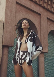 Woman wearing a brown and white patterned silk shirt and matching bottoms posing against an archway with turquoise tiles