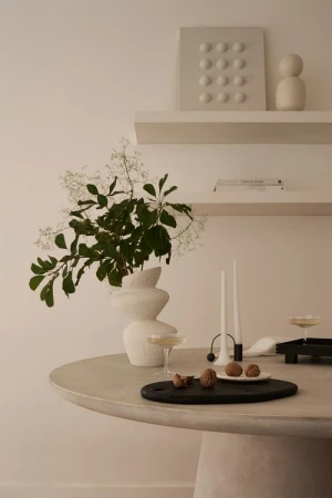 Elegant interior scene featuring a modern white vase with greenery on a round table, complemented by candles and artful wall decor.