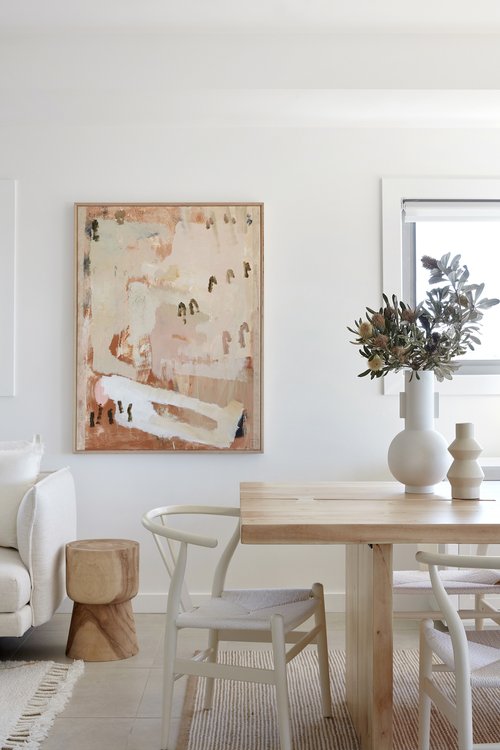 Contemporary dining room featuring a light wood table with white chairs, modern art, and natural light, creating a bright, airy atmosphere.