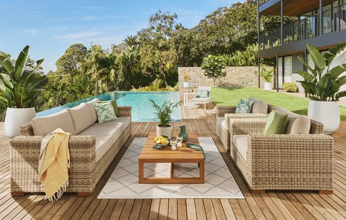 Outdoor living space featuring woven patio furniture set, including sofa and armchairs arranged around a wooden coffee table on a deck.
