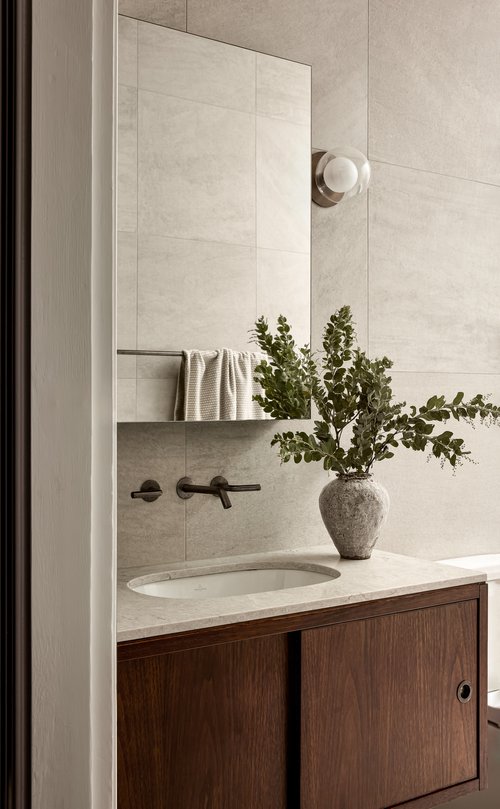 Modern bathroom interior with a vanity sink, wooden cabinet, tiled walls, a mirror, greenery, and a neutral color palette creating a spa-like ambiance.