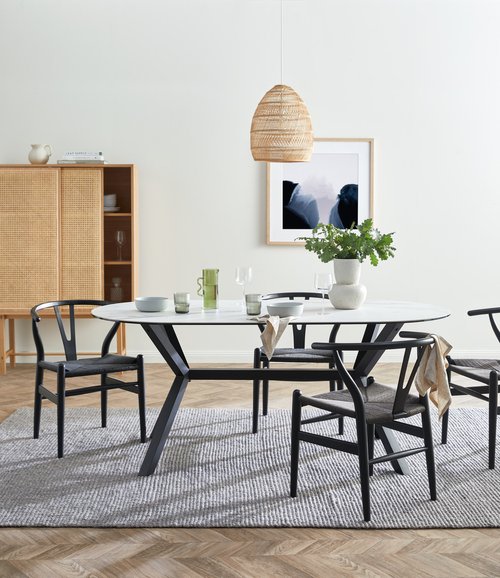Interior design featuring an oval dining table with a white marble top and black wishbone chairs, set on a gray textured rug.