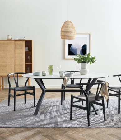 Interior design featuring an oval dining table with a white marble top and black wishbone chairs, set on a gray textured rug.