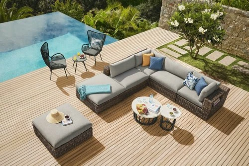 Outdoor patio arrangement with sectional sofa, lounge chairs, side tables, and a swimming pool surrounded by lush greenery.