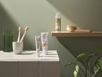 Skincare product tubes, wooden toothbrushes in a holder, and a floating shelf styled against an olive green wall.