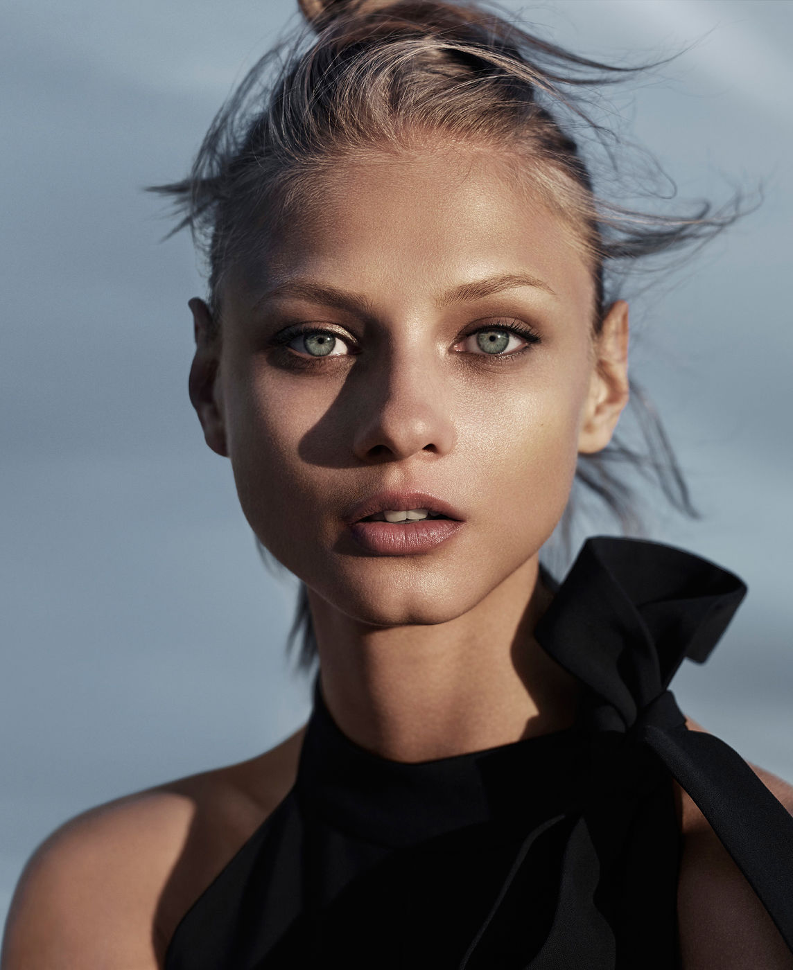 Close-up portrait of a young adult female with fair skin, green eyes, and an updo hairstyle. She wears a sleeveless black top with a bow.