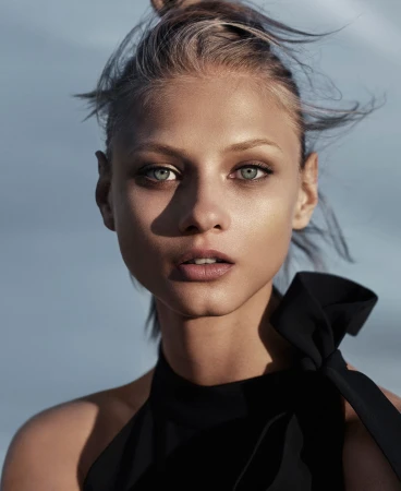 Close-up portrait of a woman with blonde hair in a black top against a blurred sky background