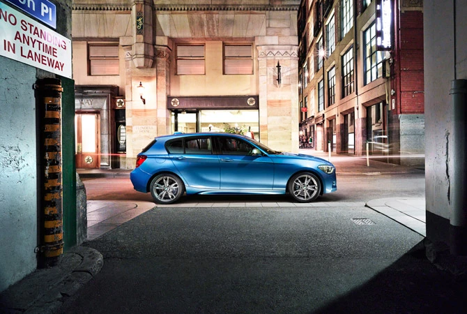 A bright blue BMW hatchback is parked on a city street at night, surrounded by urban buildings and street lights, showcasing automotive design.