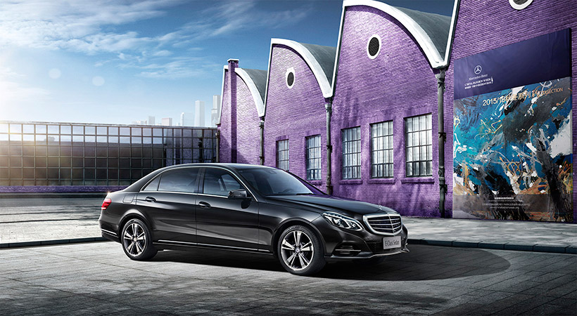 Sleek black Mercedes-Benz E-Class Sedan parked in an urban setting with a modern building and purple brick structures under a partly cloudy sky.