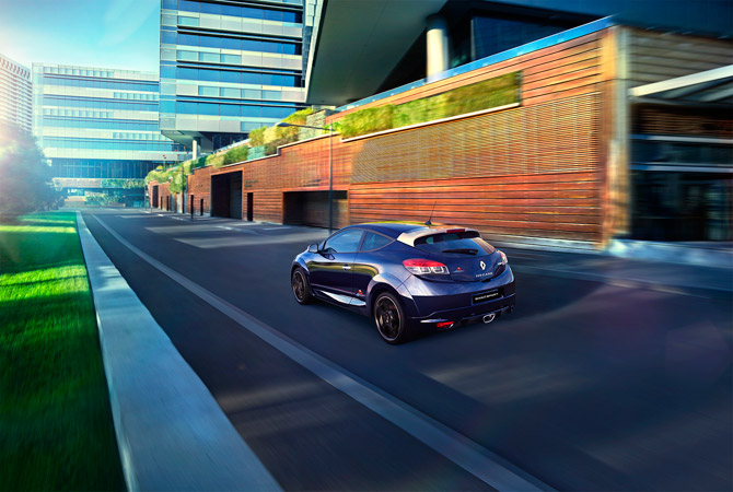 Sleek blue Renault Megane Sport coupe speeds along city street, modern architecture backdrop, sunny day, motion blur conveys speed.