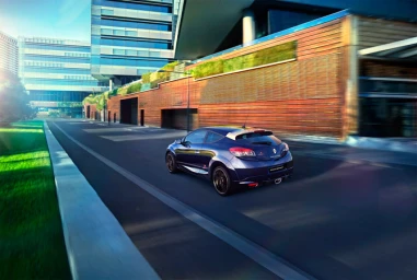 Blue hatchback car driving along a modern urban street with glass office buildings and wooden paneling.