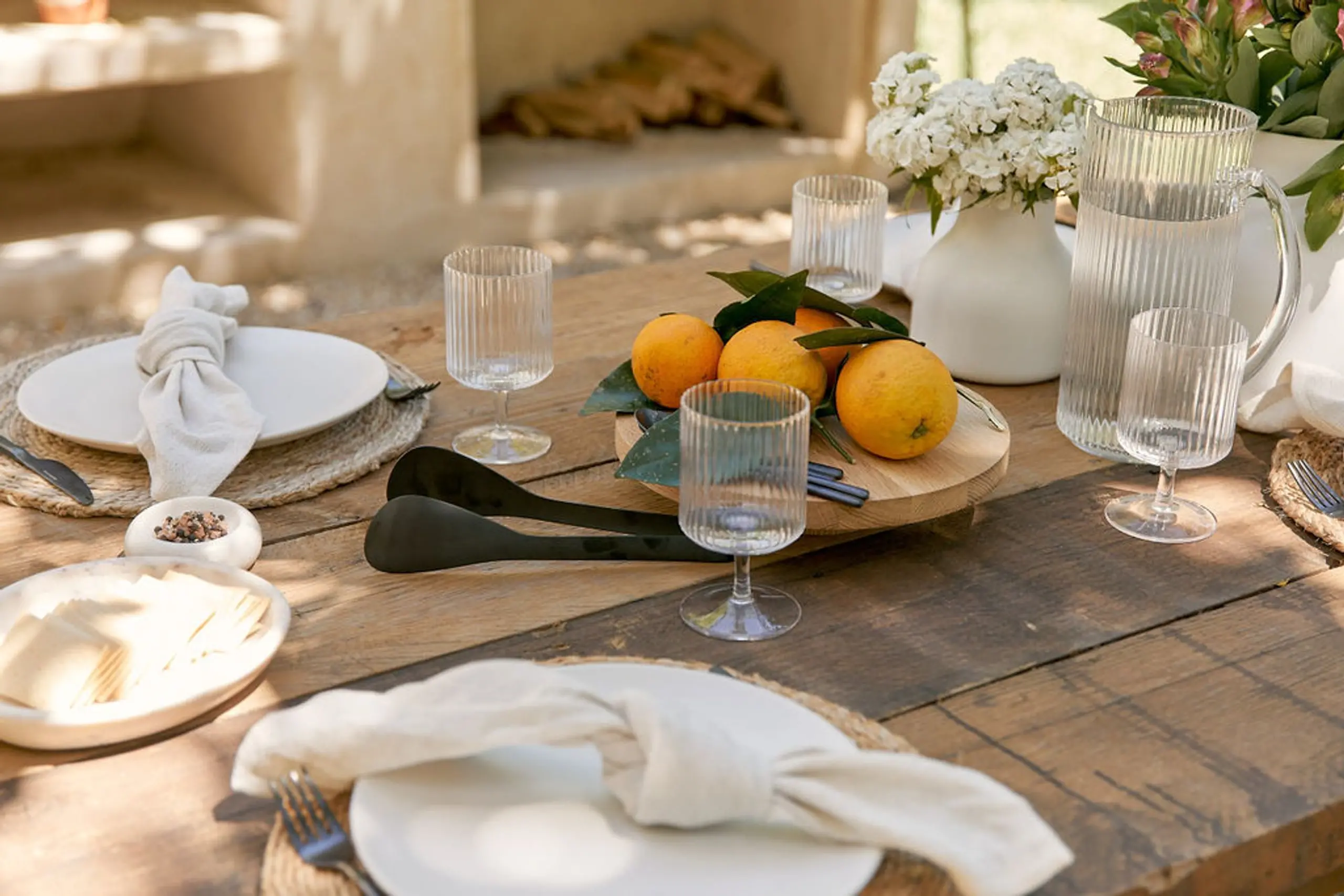 Outdoor table setting features plates, napkins, glassware, and oranges, creating an inviting and elegant ambiance for al fresco dining.