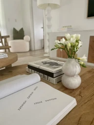 White flowers in a ceramic vase on a wooden coffee table styled with books in a bright living room