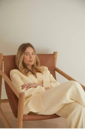 Woman with blonde hair wearing a cream-colored pantsuit seated in a wooden leather chair.