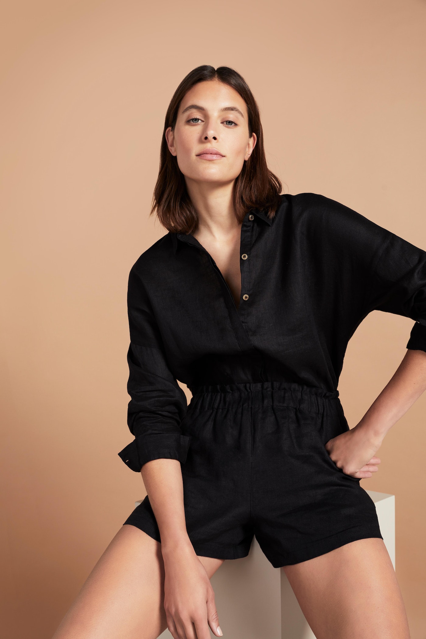Portrait of a woman wearing a black collared shirt and shorts, posing indoors with her hand in her pocket in a studio setting.